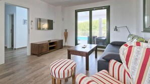 Un salon comprenant un canapé, des fauteuils, une table basse, un téléviseur et une porte-fenêtre coulissante donnant sur un balcon.