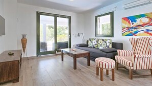 Un salon moderne avec un canapé, un fauteuil à rayures et un pouf, une table basse en bois et un grand lampadaire.