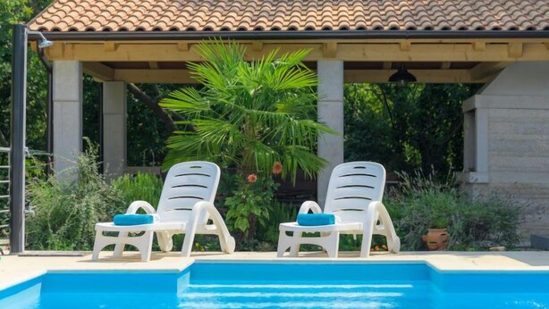 Une piscine avec deux chaises longues blanches et une pergola surmontée d’un toit en tuiles.