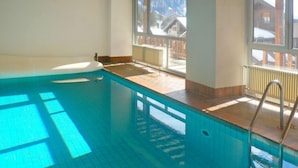 Una piscina interior amb vistes clares a un paisatge muntanyós cobert de neu a través de grans finestres.