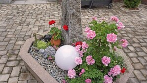 Een tuin met een stenen constructie, roze bloemen en een witte bol.