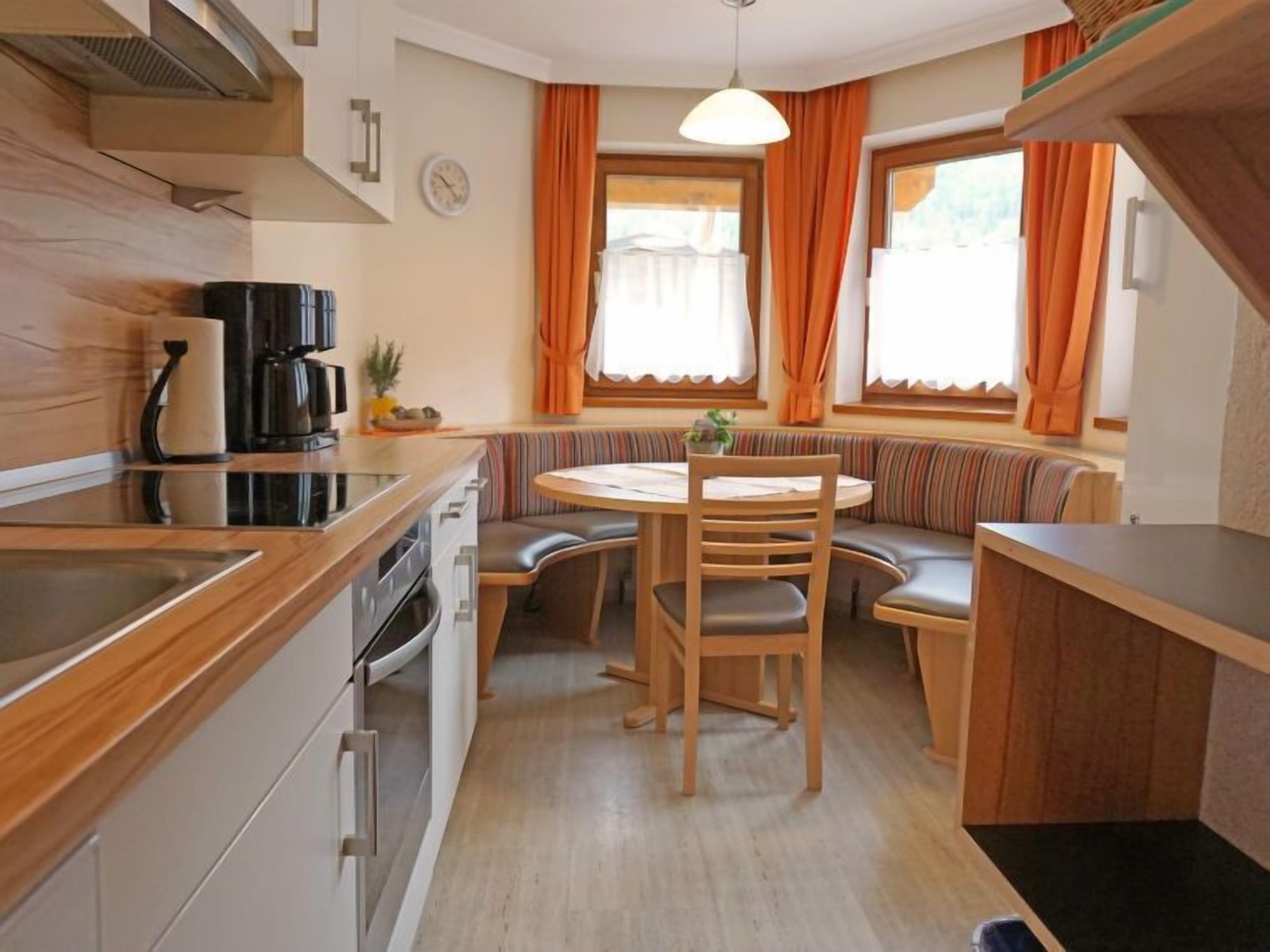 A compact kitchen with a wooden countertop, a stove, and a sink. There is a round table with chairs and a bench along the wall.