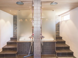 A modern bathroom with a central column, two showerheads, and a stone accent wall. - Holy lake chalet b by Interhome (Kuusamo)
