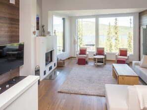 Un salon moderne doté d’une cheminée, d’un coin salon et de grandes fenêtres offrant une vue sur les arbres et les collines.