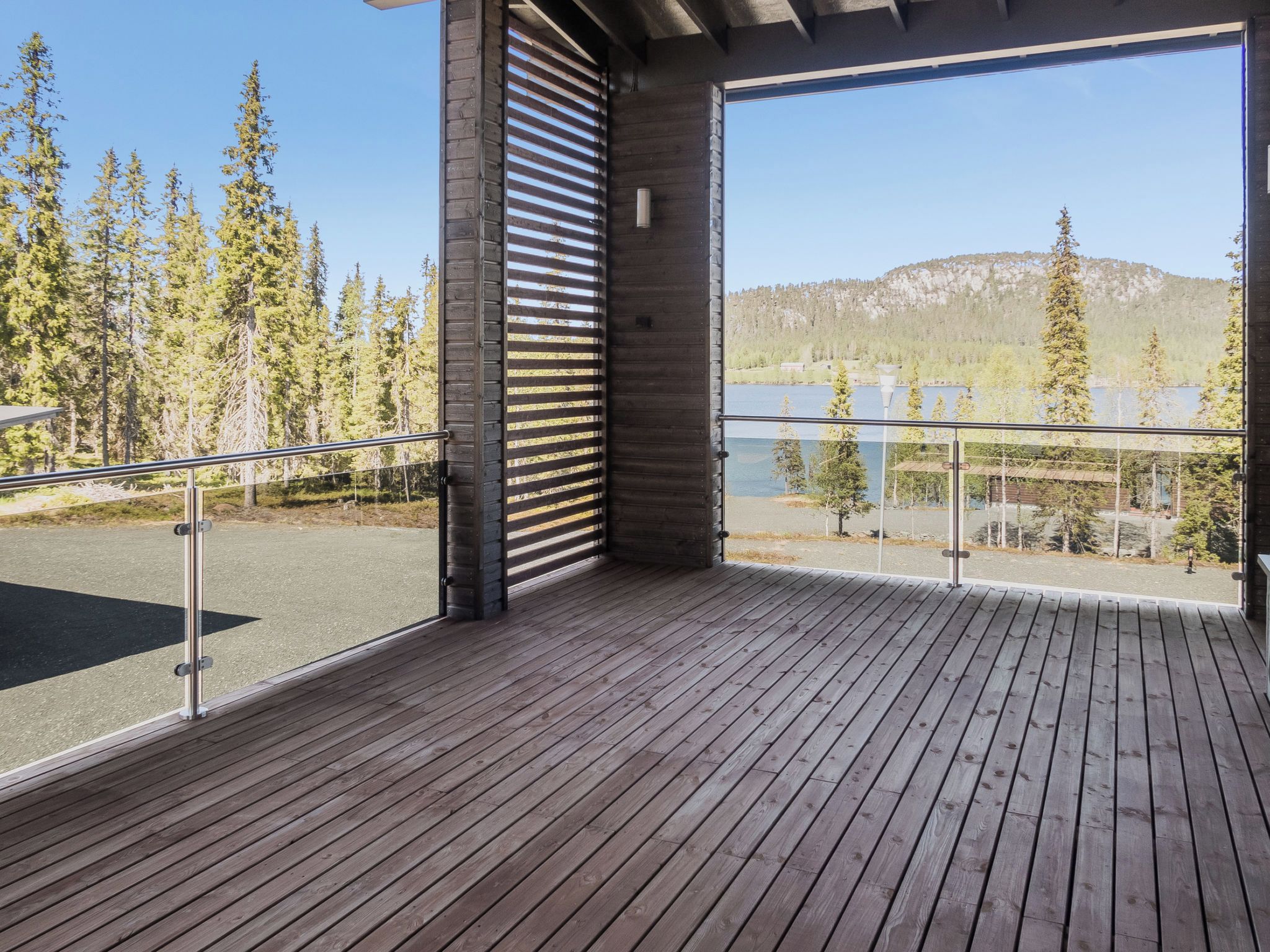 Una terraza de madera con barandilla de vidrio que da a un lago y un bosque.