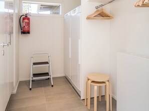 Un baño limpio y moderno con suelo de baldosas blancas, cabina de ducha blanca, un taburete de madera y una escalera metálica.