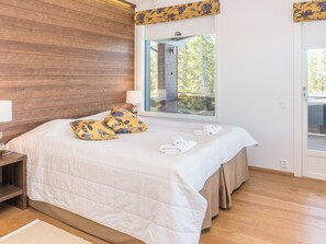 Een slaapkamer met een groot bed, houten wanden, een raam met uitzicht en een deur.