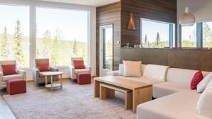 Een moderne woonkamer met een groot raam, houten vloeren en een beige bank.