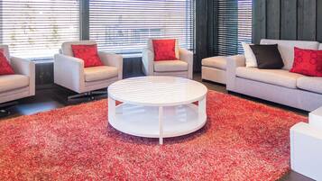 A modern living room with a round coffee table, sofas, and armchairs, featuring a red shag carpet.