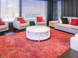 Un salon moderne avec une table basse ronde, des canapés et des fauteuils, agrémenté d’un tapis rouge à longues mèches.