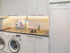 Una cocina moderna con lavadora integrada, un lavamanos de acero inoxidable y diversos productos de limpieza en la encimera.