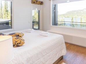 A bedroom with a large bed, a window with a view of trees and a lake, and a wooden floor. - Holy lake chalet b by Interhome (Kuusamo)