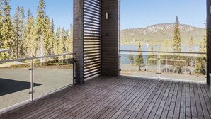 Een houten terras met glazen hekwerk, met uitzicht op een meer en beboste bergen.