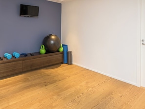 A room with a wooden floor, a wall-mounted TV, exercise equipment, and a door. - Holy lake chalet b by Interhome (Kuusamo)