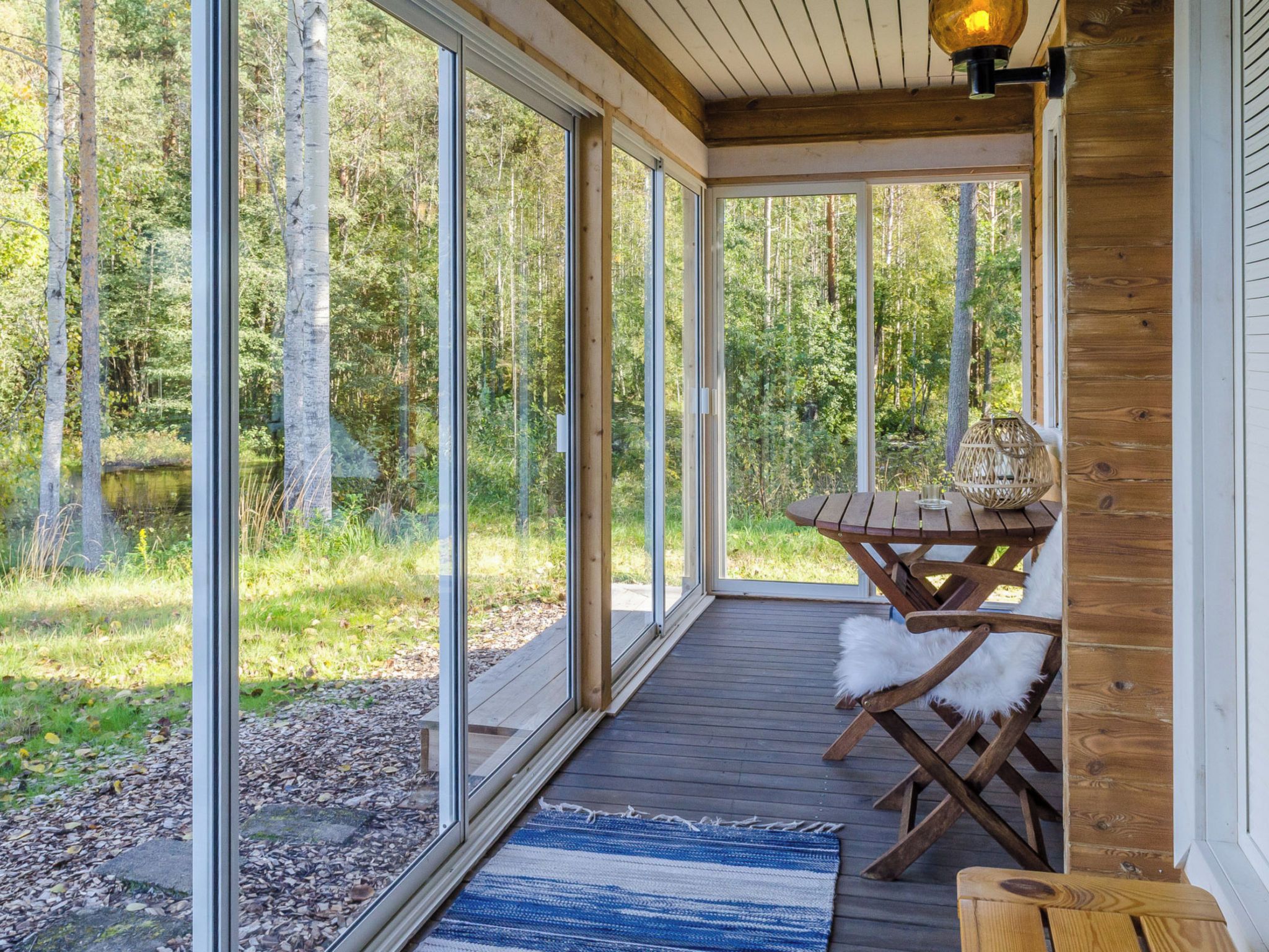 A covered outdoor area with a wooden deck, a table with chairs, and a view of a forest.