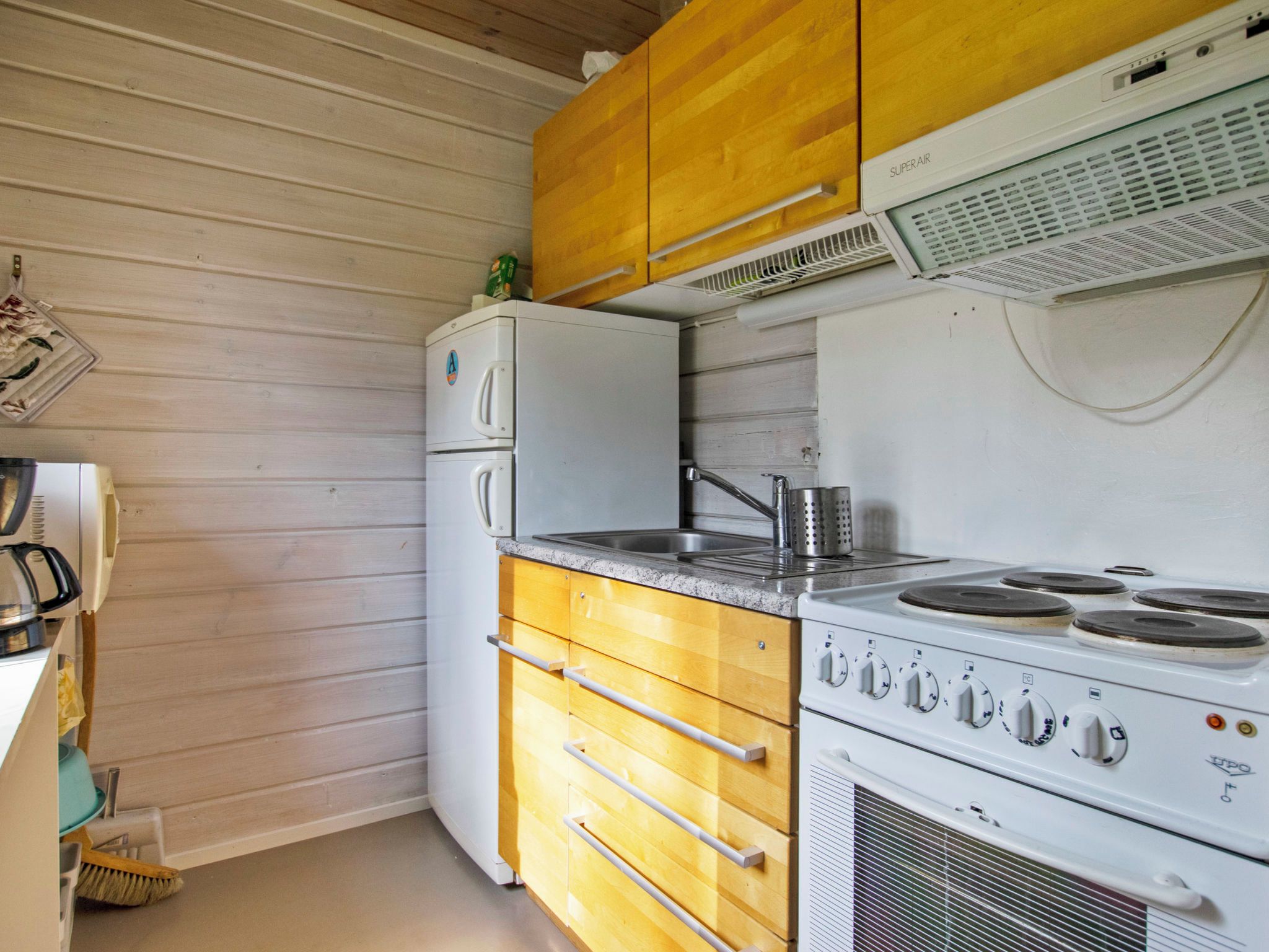 Cocina compacta con muebles de madera, un refrigerador blanco, una estufa de cuatro quemadores y un fregadero.