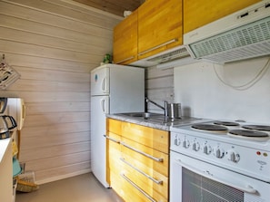 Cocina compacta con muebles de madera, un refrigerador blanco, una estufa de cuatro quemadores y un fregadero.