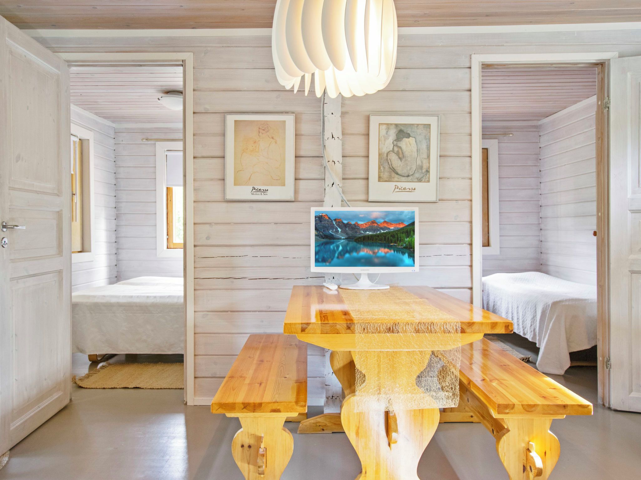 A room with a wooden table, two beds, and artwork on the walls.