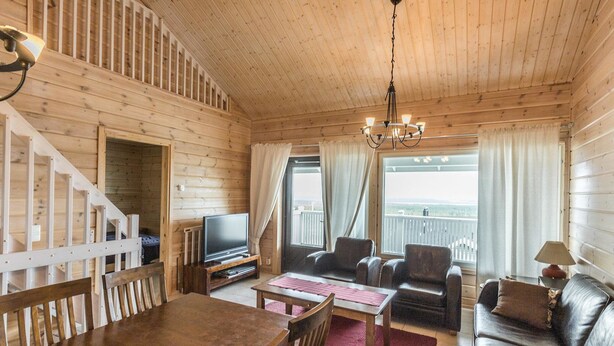 Ein Holzblockhaus-Innenraum mit Essbereich, Wohnzimmer und einem Balkon mit Blick.