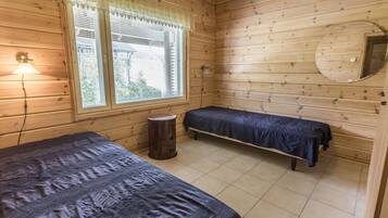 Una cabaña con dos camas, un taburete pequeño, una ventana con persianas, una lámpara y un espejo en la pared.