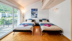 A modern bedroom with two beds, a large window, and a view of a town.