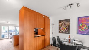 A modern kitchen with a wooden cabinet, a dining area with a table set for two, and a large window.