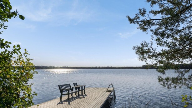 A wooden dock extending into calm water, with two benches and a small table, surrounded by lush greenery. - Kärkiniemi by Interhome (Tuusniemi)