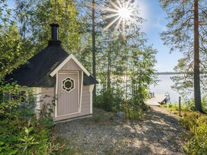 Une petite cabane avec une cheminée, une porte ornée d’un vitrail et un chemin de gravier menant à un quai au bord d’un lac.