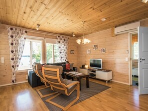 Una habitación con paneles de madera, un sofá, sillas, un televisor y una mesita.