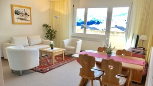 A living room with a sofa, a coffee table, and a dining table with chairs. There is a window with a view of a snowy landscape. - Disentiserhof Hönig by Interhome (Disentis)