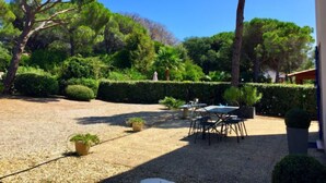 Un'area patio esterna con fondo in ghiaia, circondata da siepi e alberi ben curati. Sono disposti tavoli e sedie per mangiare o socializzare.