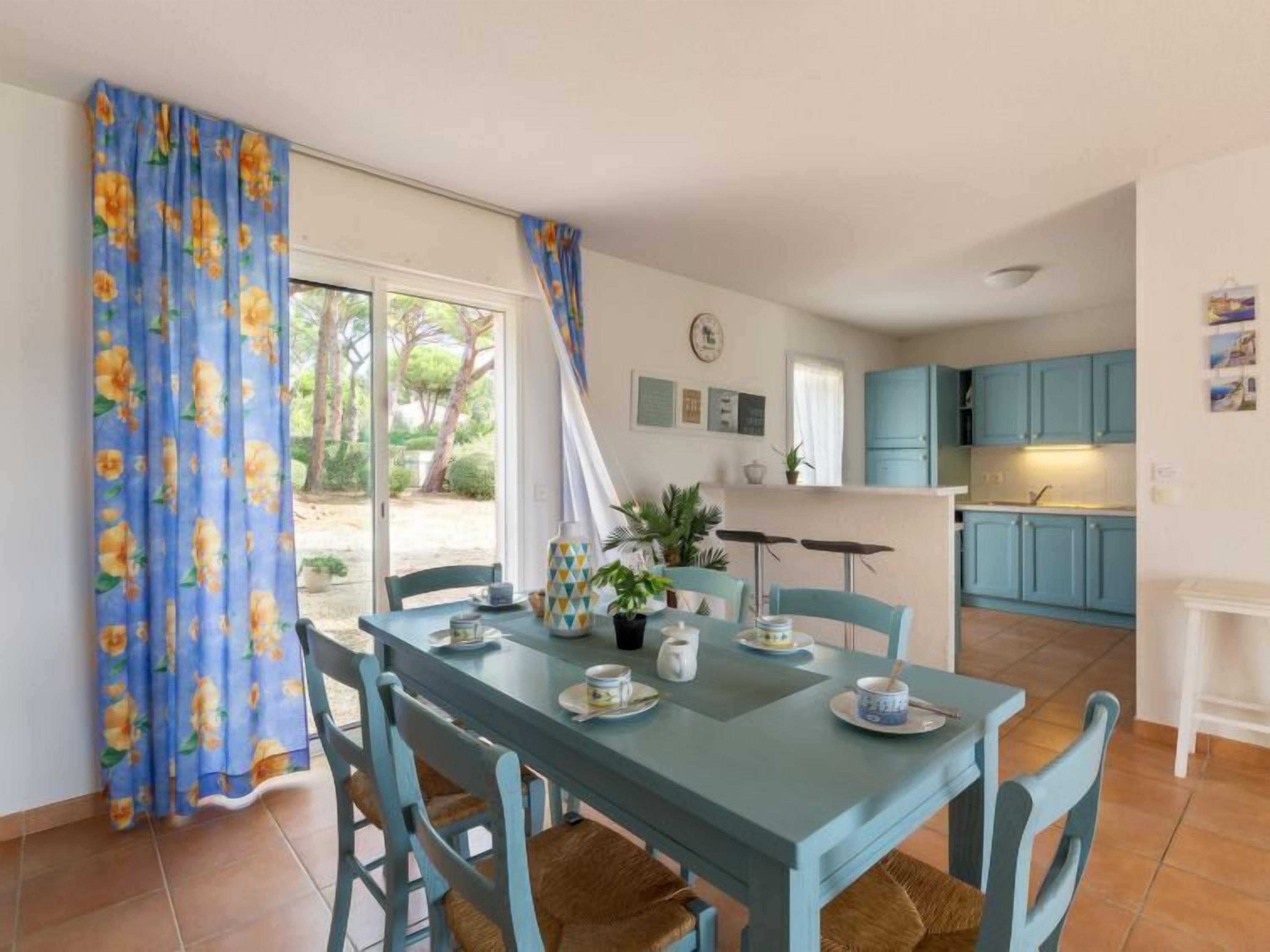 A dining area with a table set for four, blue chairs, and a view of a kitchen with blue cabinets.