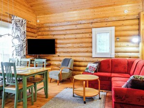 L’intérieur d’un chalet confortable, avec une salle à manger, un téléviseur et un canapé rouge.