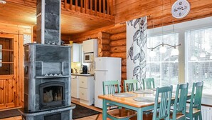 L’intérieur chaleureux d’un chalet avec une cheminée en pierre, une table à manger en bois, des chaises de couleur turquoise et un coin cuisine doté d’appareils électroménagers blancs.