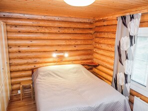Een blokhutkamer met een bed, een klein krukje en een raam met gordijnen.
