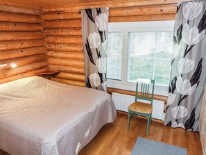 Een blokhutkamer met een bed, een stoel, een raam met zonwering en een radiator.