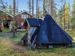 Une cabane en rondins, dotée d’un toit à forte pente, entourée d’une forêt.
