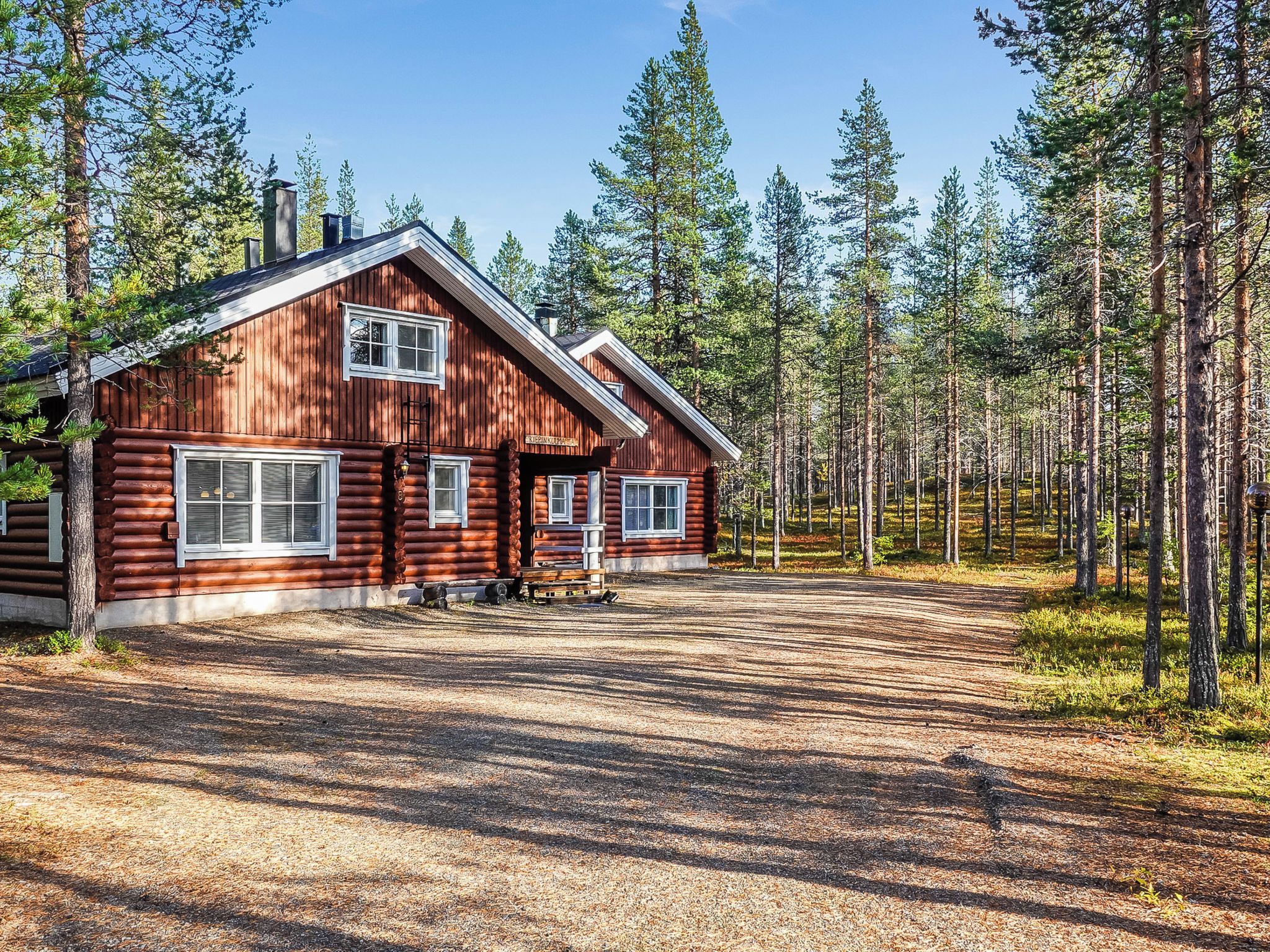 A log cabin with a chimney, a porch, and a clear view of a forested area.