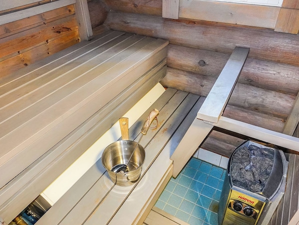 Een sauna met een metalen kom, een houten bank en een sauna-oven.