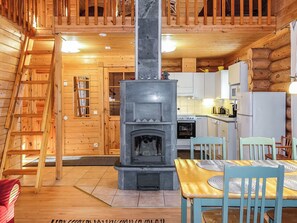 Un intérieur en bois avec une cheminée centrale, un coin repas avec des chaises et une cuisine équipée.