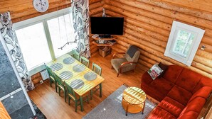 L’intérieur d’un chalet accueillant comprend un coin repas, un salon avec un canapé rouge, un téléviseur et une horloge murale.