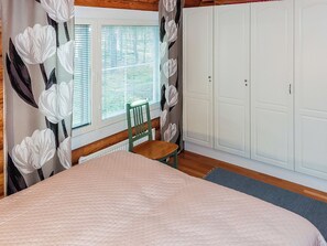 Une chambre à coucher avec un lit, une chaise, une fenêtre avec des stores et une armoire.