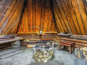 Interieur van een blokhut met een vuurplaats van natuursteen, houten banken en een raam met uitzicht.