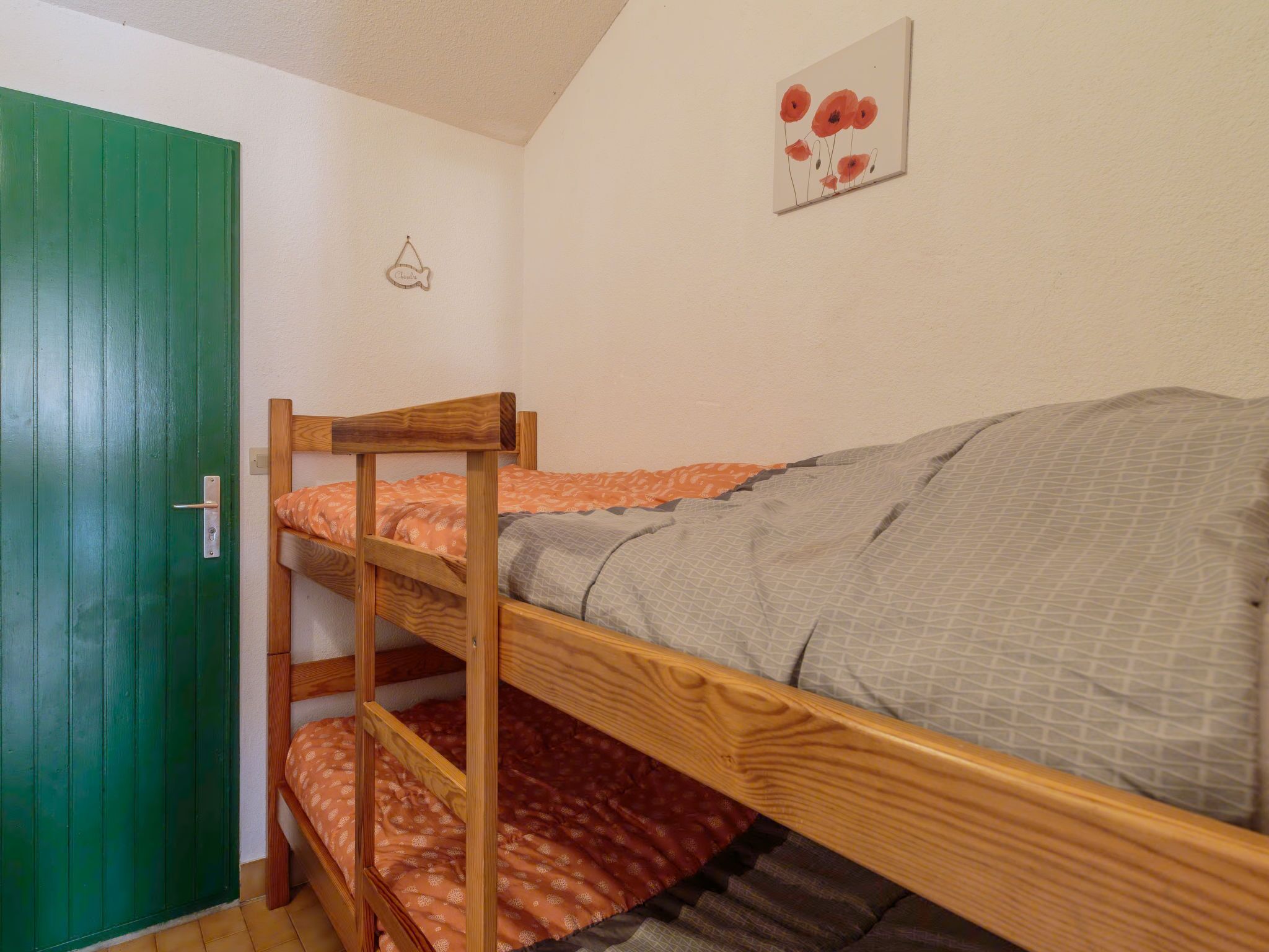 Habitación con literas, una puerta verde, un adorno con forma de pez y un cuadro en la pared.