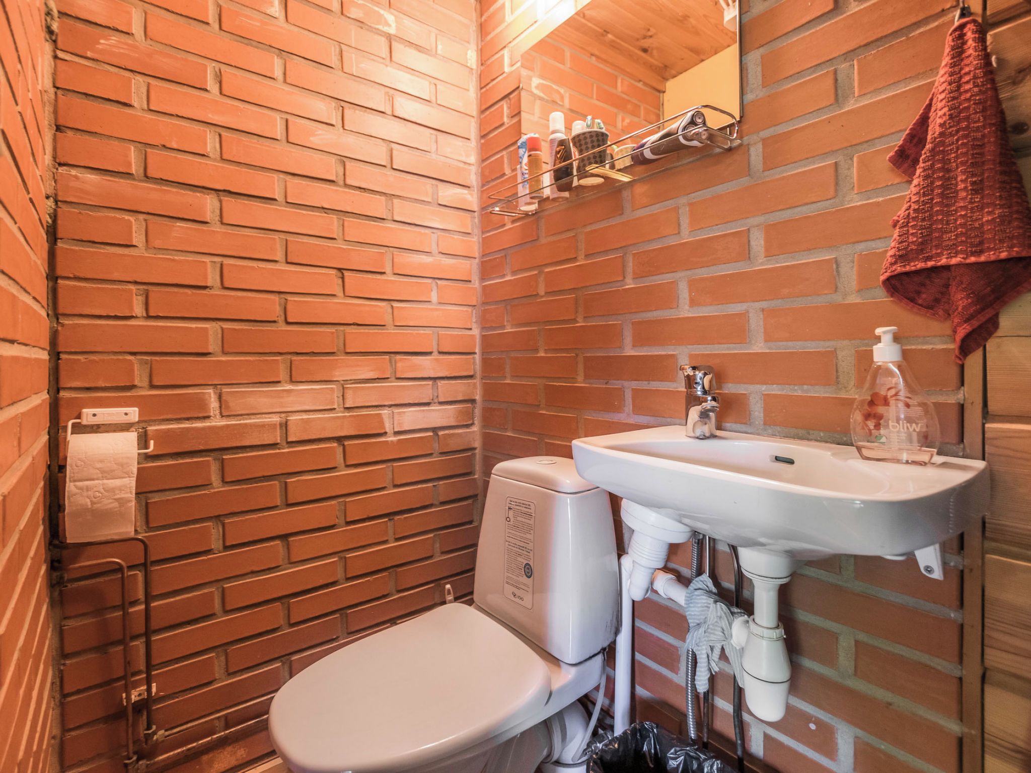 Un baño pequeño y funcional con un inodoro blanco, un lavamanos blanco y una toalla roja colgada en la pared.