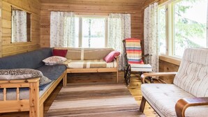 L’intérieur d’un chalet accueillant, avec un plafond en bois, un canapé, un fauteuil et une fenêtre agrémentée de rideaux.