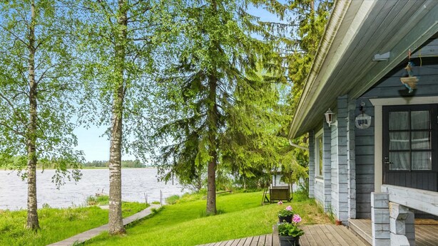 Un chalet au bord du lac, doté d’une terrasse en bois, d’un petit jardin fleuri et offrant une vue sur le lac.