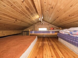 Un pequeño dormitorio en el ático con paredes de madera y techo inclinado, con dos camas y una ventana.