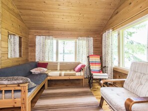 Ein gemütliches Zimmer mit Holzbalkendecke, einer Couch, einem Schaukelstuhl und einem Fenster mit Vorhängen.