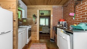 Une cuisine compacte aux murs en bois, dotée d’une cheminée en briques et d’un petit coin repas visible à travers une porte ouverte.
